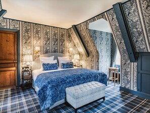 A bedroom with a bed, two bedside tables, a bench, and patterned wallpaper. - Abbaye Des Vaux De Cernay (Cernay-la-Ville)
