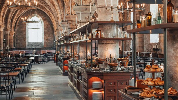 A spacious hall with high arched ceilings, rows of tables, and a central serving area with food displays.