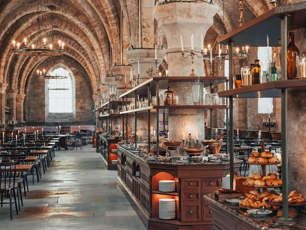 A spacious hall with high arched ceilings, rows of tables, and a central serving area with food displays.