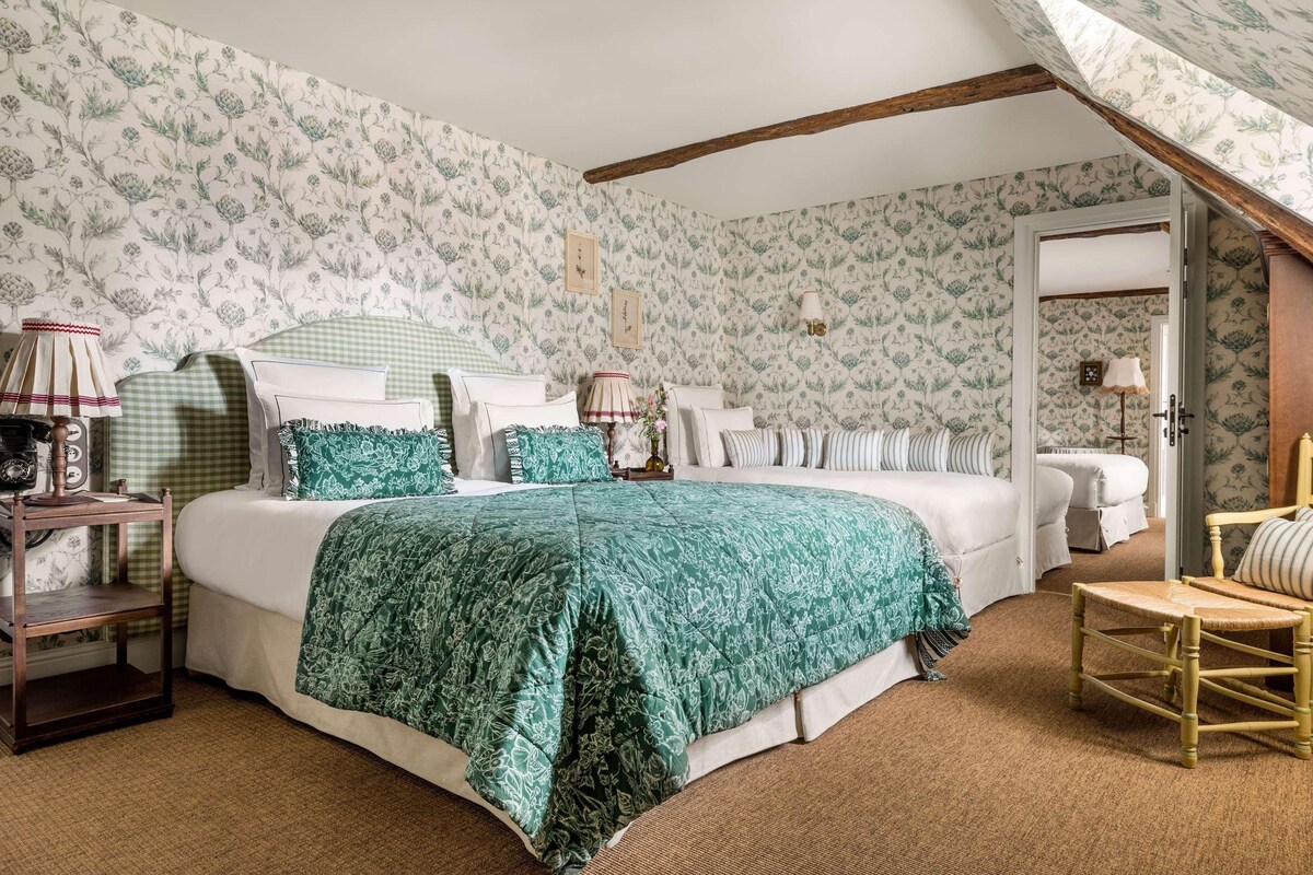 A bedroom with a large bed, a wooden chair, a nightstand, and a lamp.