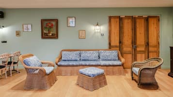 Quarto com sofá, duas cadeiras de vime, uma mesa de madeira e uma porta grande de madeira.