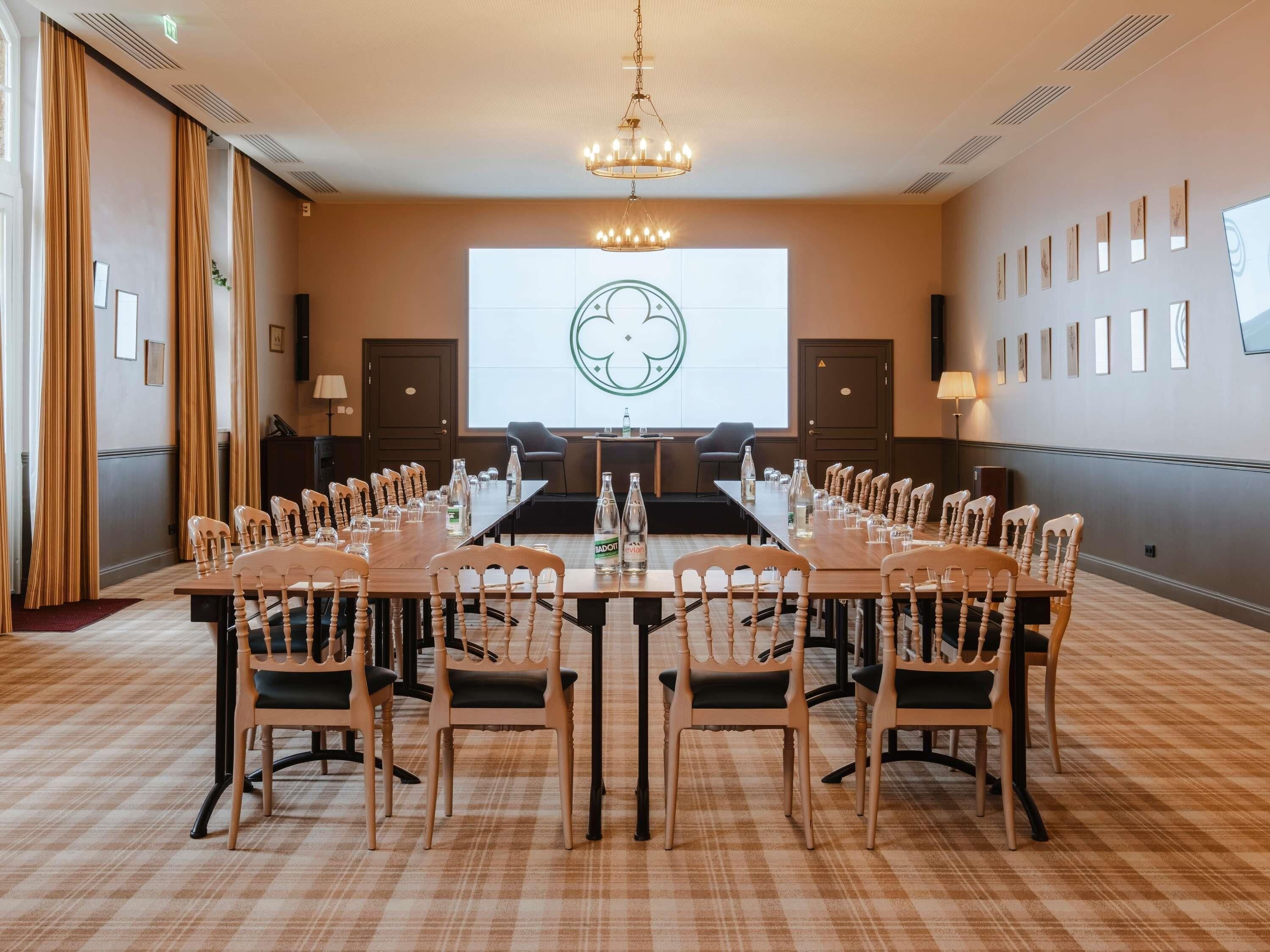A conference room with a long table, chairs, a projector screen, and a chandelier.