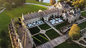 A large, historic building with multiple wings, a central courtyard with outdoor seating, and a surrounding lush landscape.
