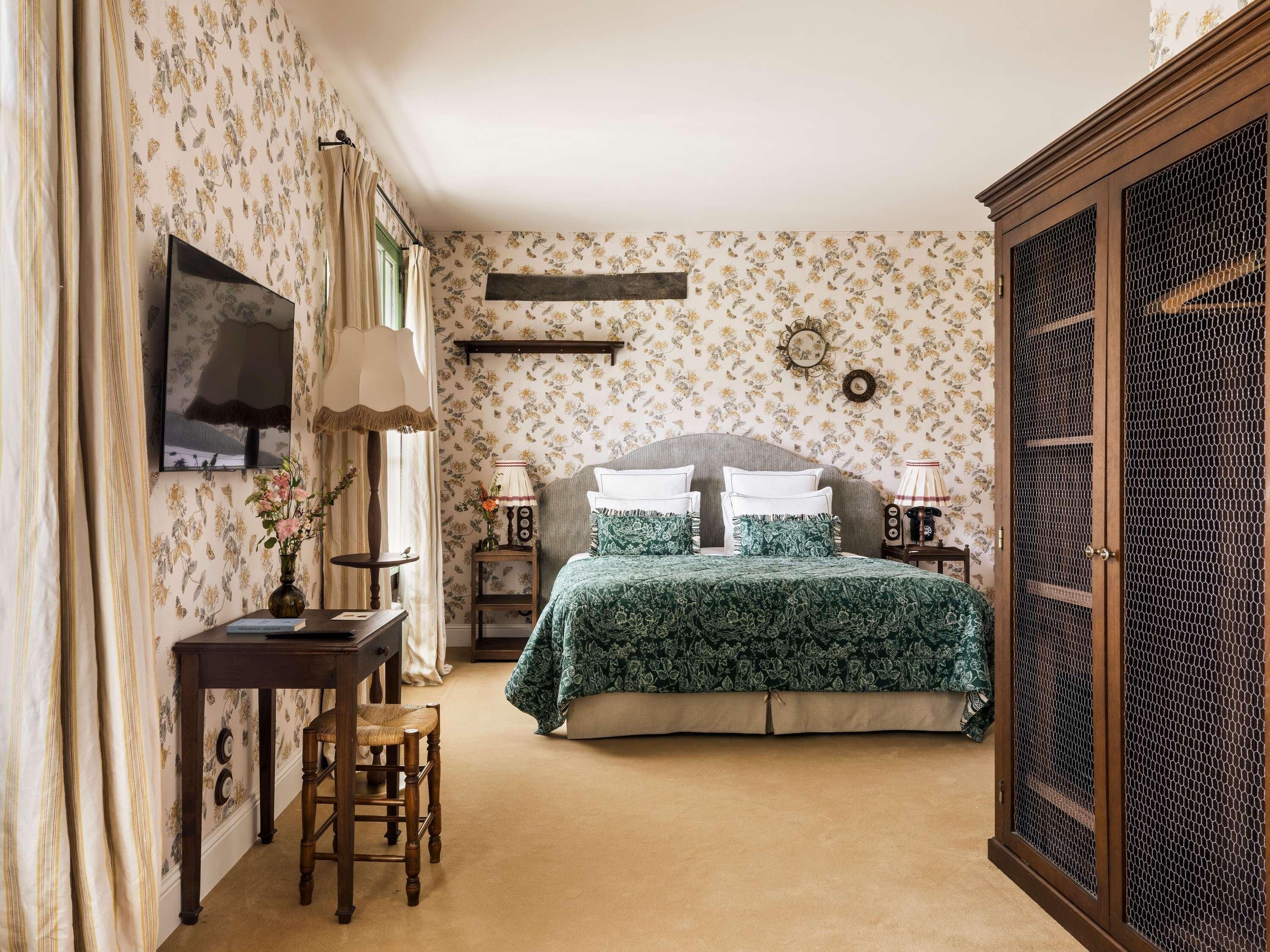 A bedroom with a bed, bedside tables, a desk, a chair, a wardrobe, and a television.