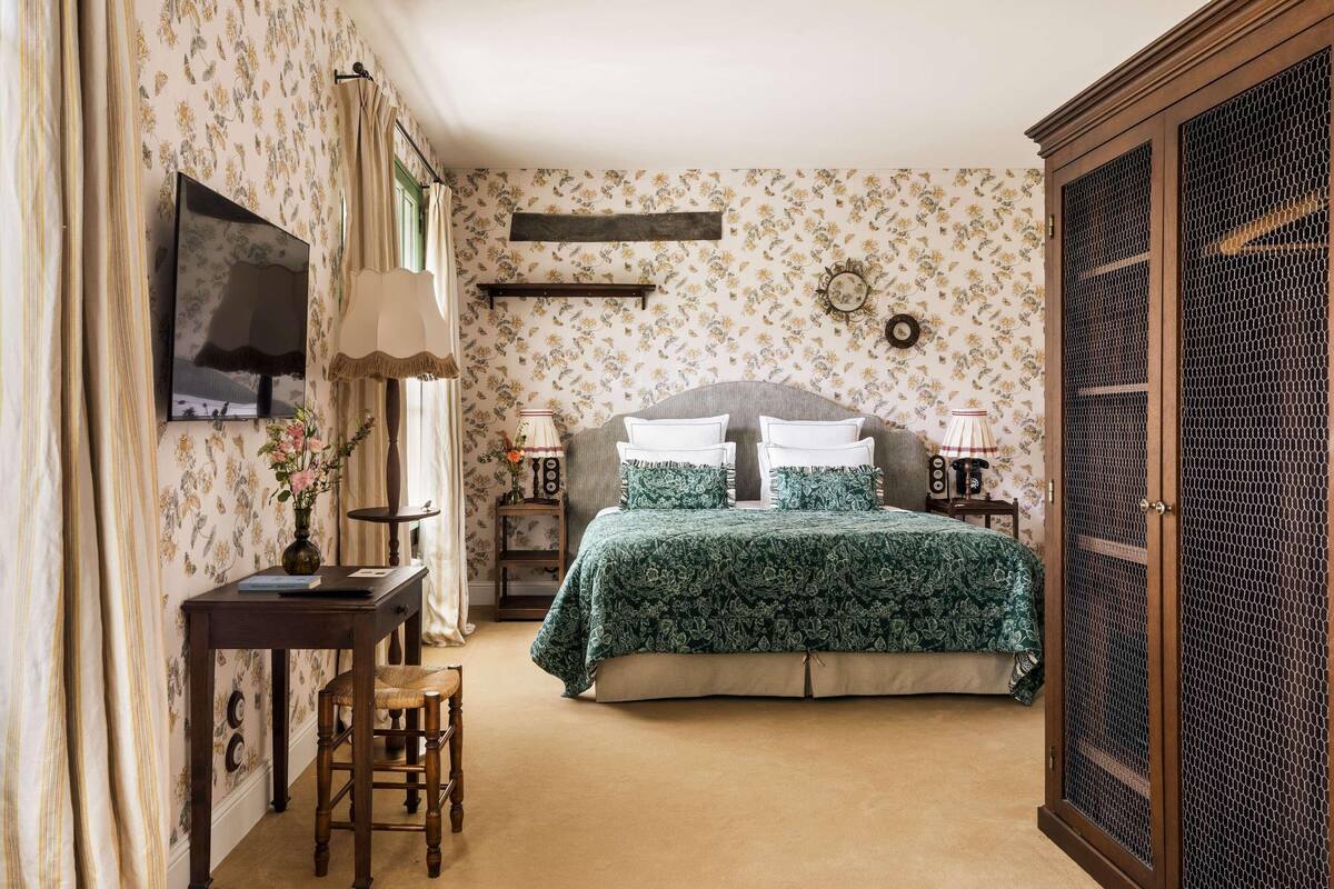 A bedroom with a bed, bedside tables, a desk, a chair, a wardrobe, and a television.