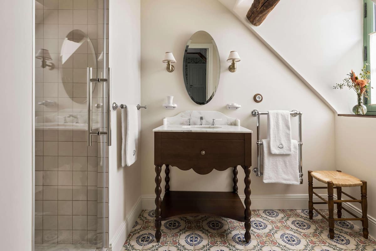 A bathroom with a glass shower enclosure, a wooden vanity with a marble countertop, and a patterned tile floor.