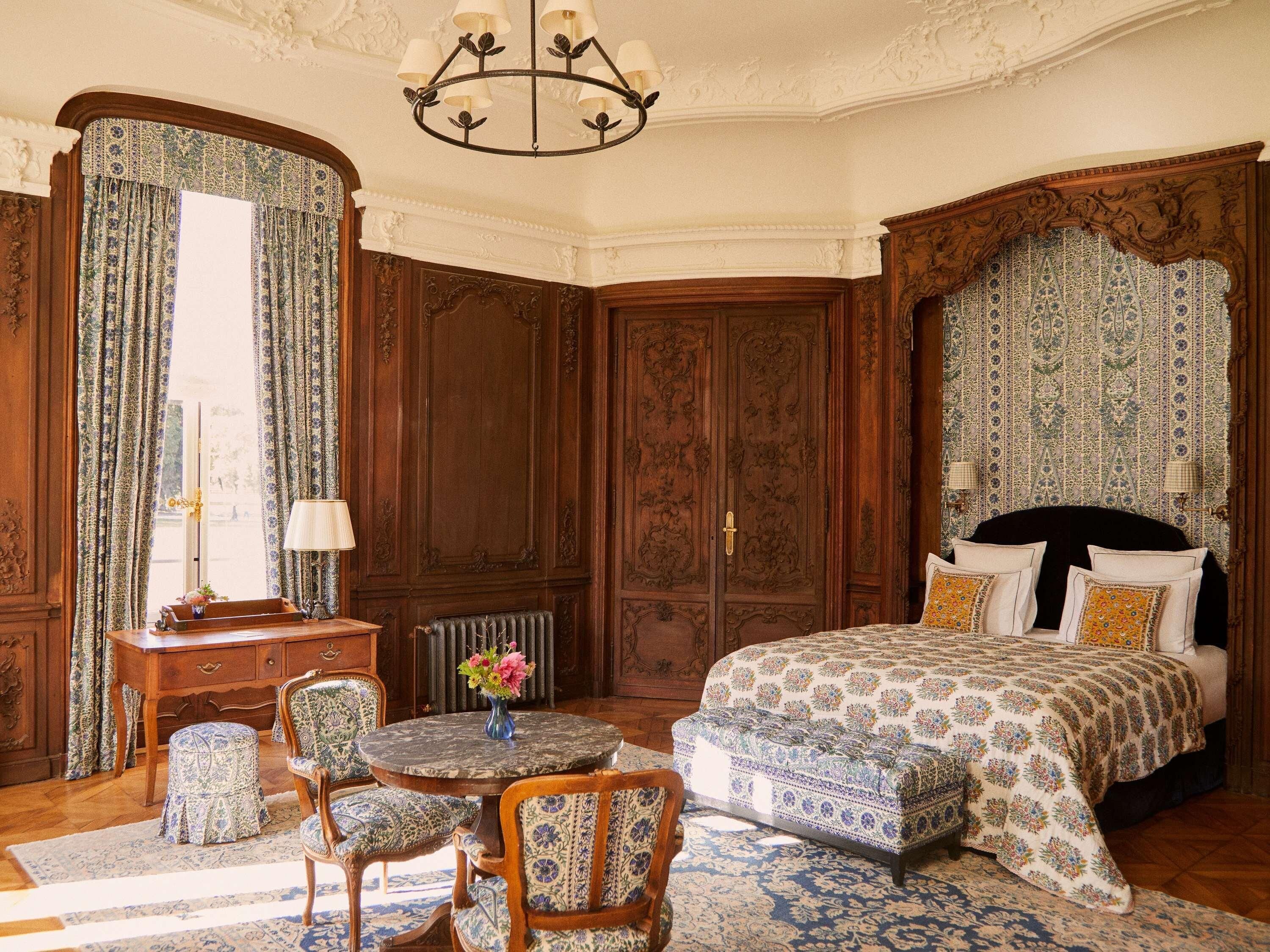 Een klassieke kamer met een bed, een ronde tafel, stoelen, een bureau en een radiator.