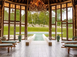 A wooden gazebo with a pool, benches, and potted plants.