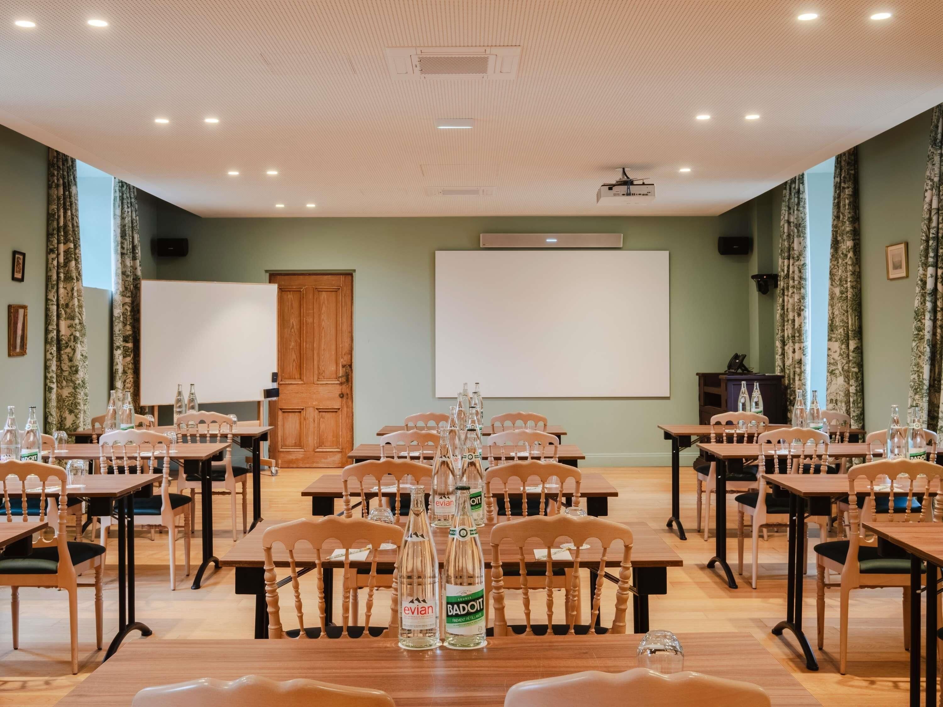 A conference room with tables, chairs, a projector, and a whiteboard.