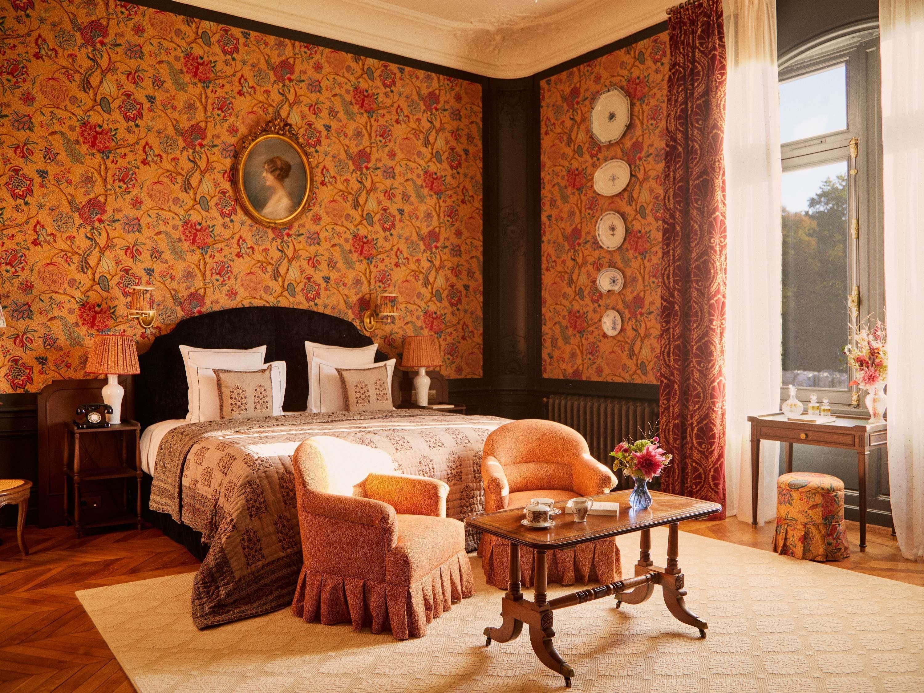 A bedroom with a large bed, a chair, a table, and a window with curtains.