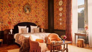 A bedroom with a large bed, a chair, a table, and a window with curtains.