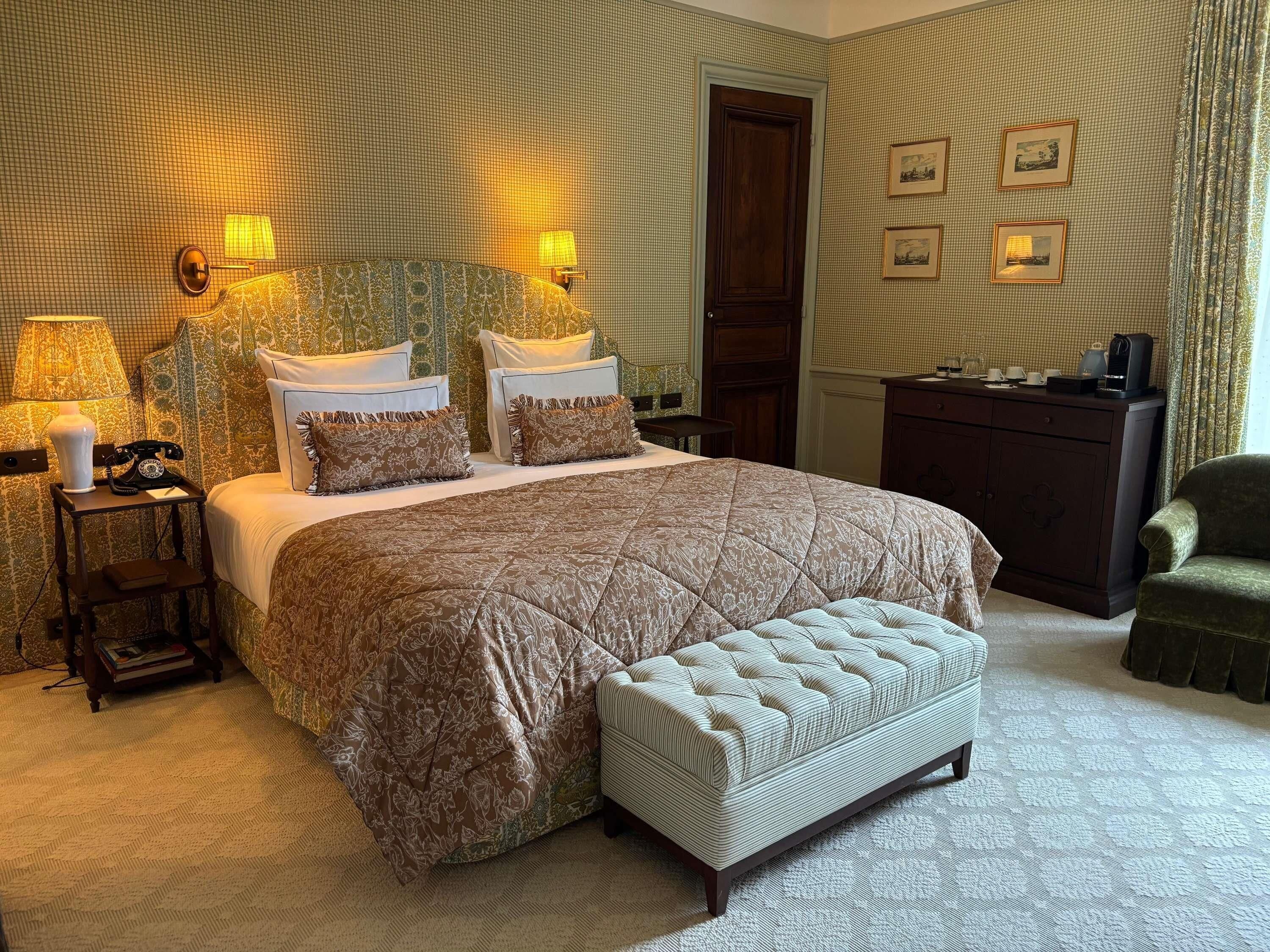 A bedroom with a large bed, bedside lamps, a wooden dresser, and a green armchair.