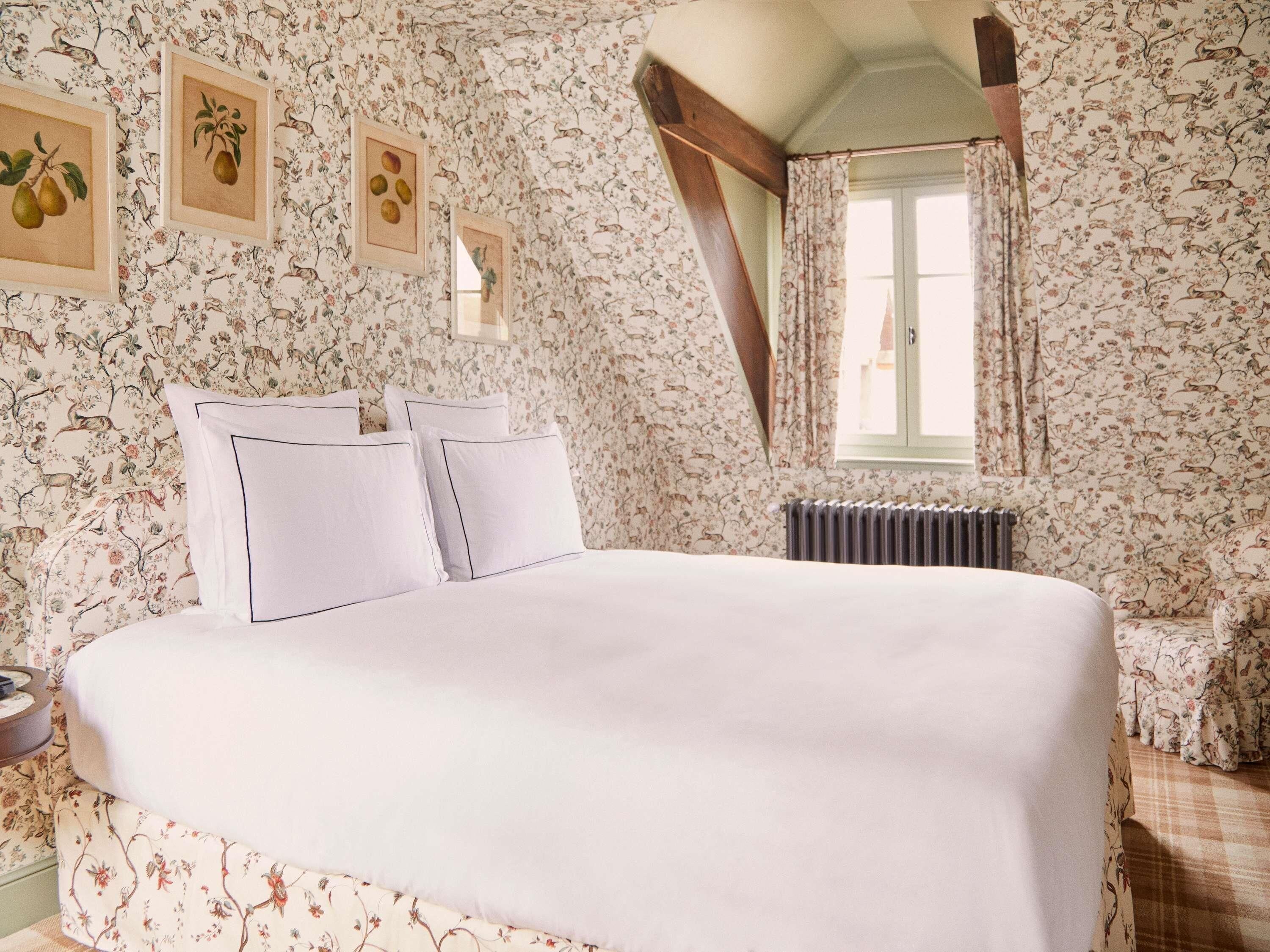 A bedroom with a large bed, floral wallpaper, a radiator, and a window with curtains.