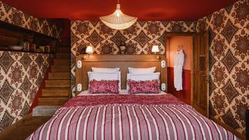 A hotel room with a large bed, a wooden headboard, a chandelier, a staircase, and patterned wallpaper.