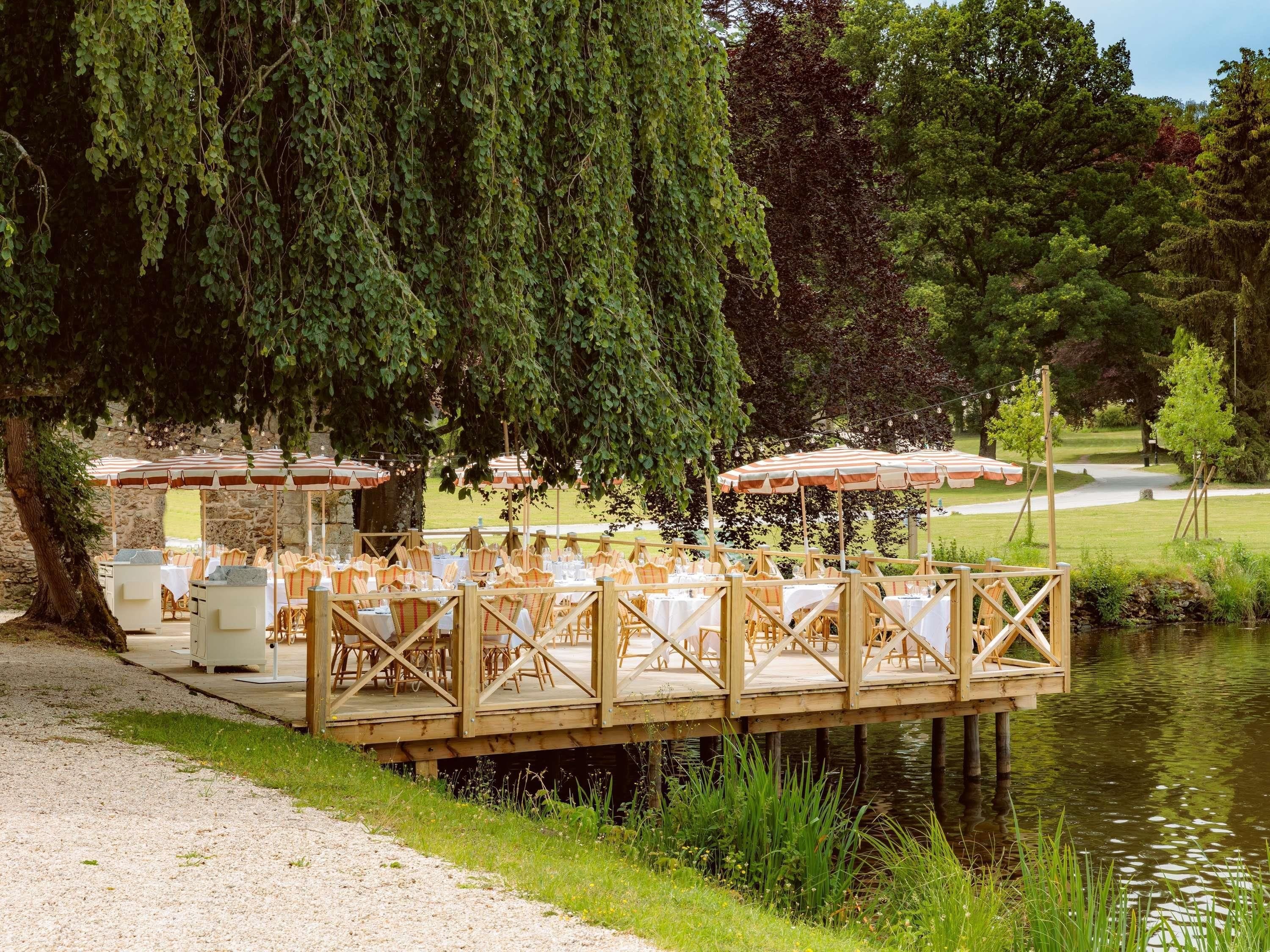A wooden deck with tables and chairs, overlooking a body of water.