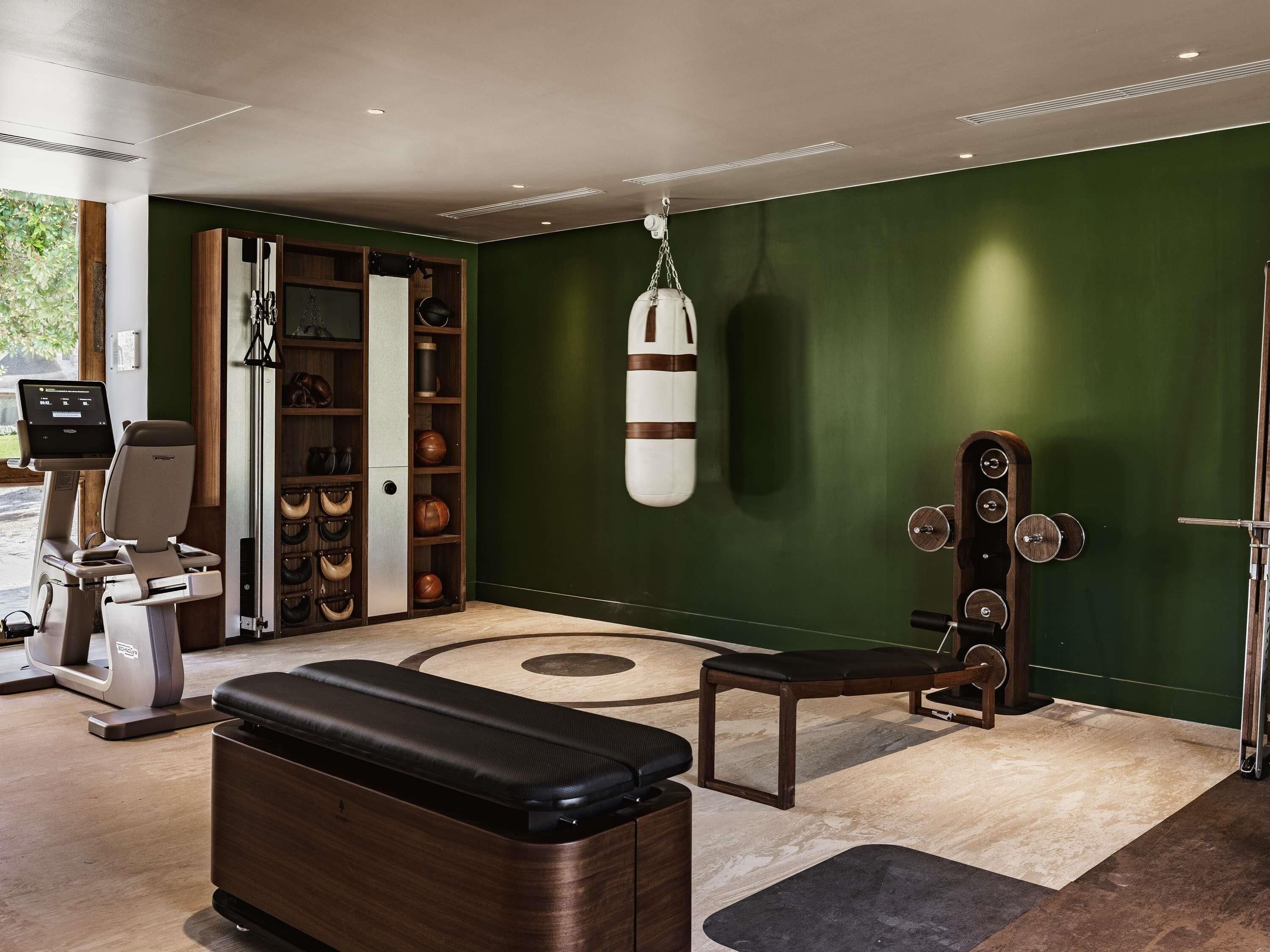 A fitness room with exercise equipment, a punching bag, a bench, and a wall-mounted rack.