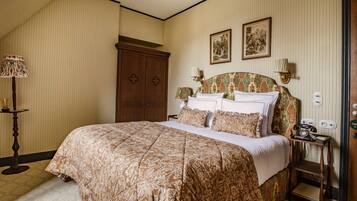 A bedroom with a large bed, a wooden wardrobe, a nightstand with a telephone, and two framed pictures on the wall.