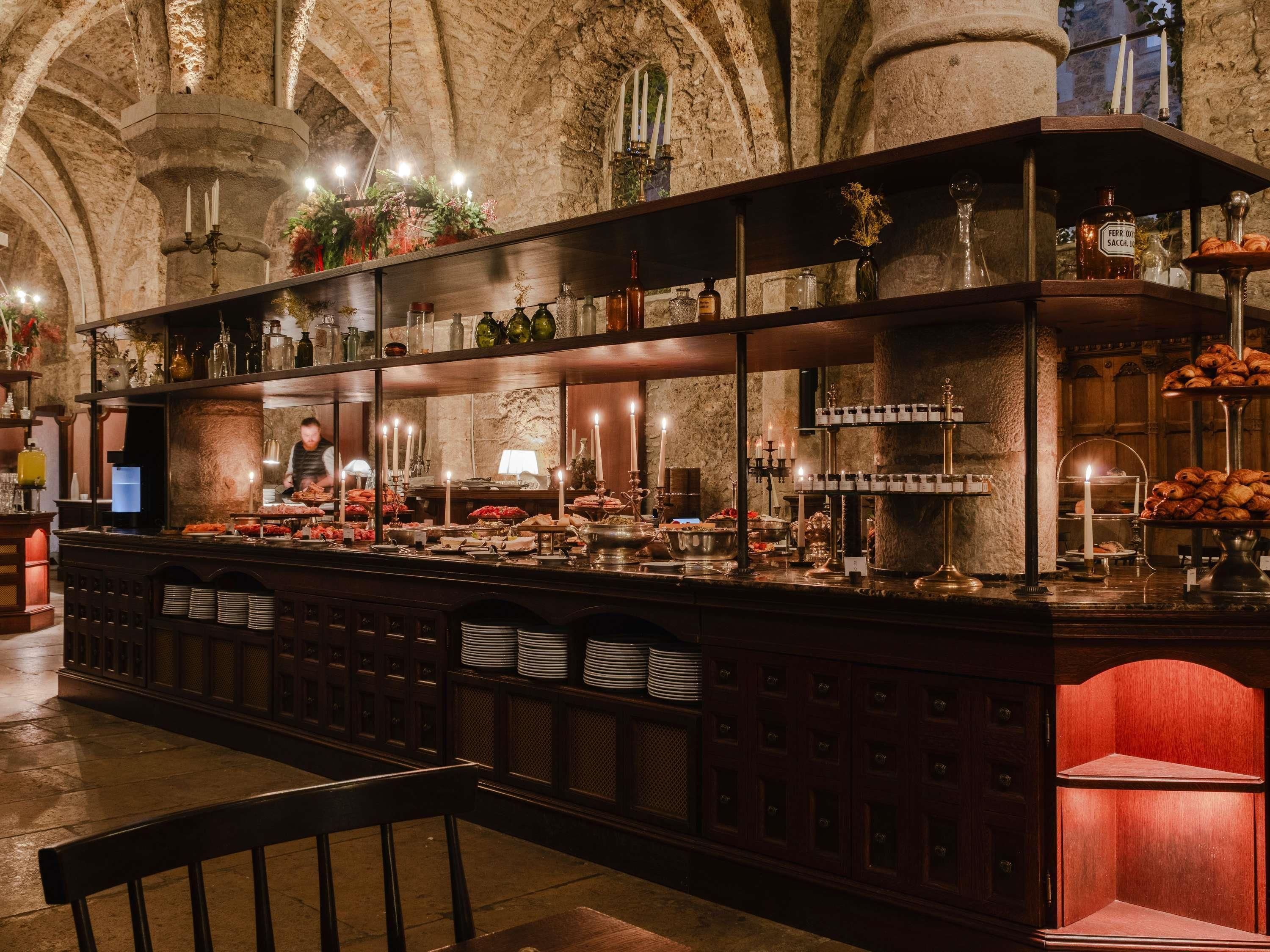 Un'area bar con una parete in pietra a fare da sfondo, scaffali con diverse bottiglie e un'esposizione di pasticceria.