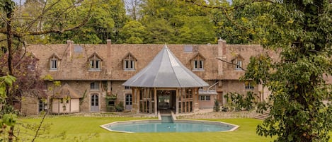Un grand bâtiment en briques, doté d’un pavillon central à toit de verre, d’une piscine et d’une pelouse bien entretenue.