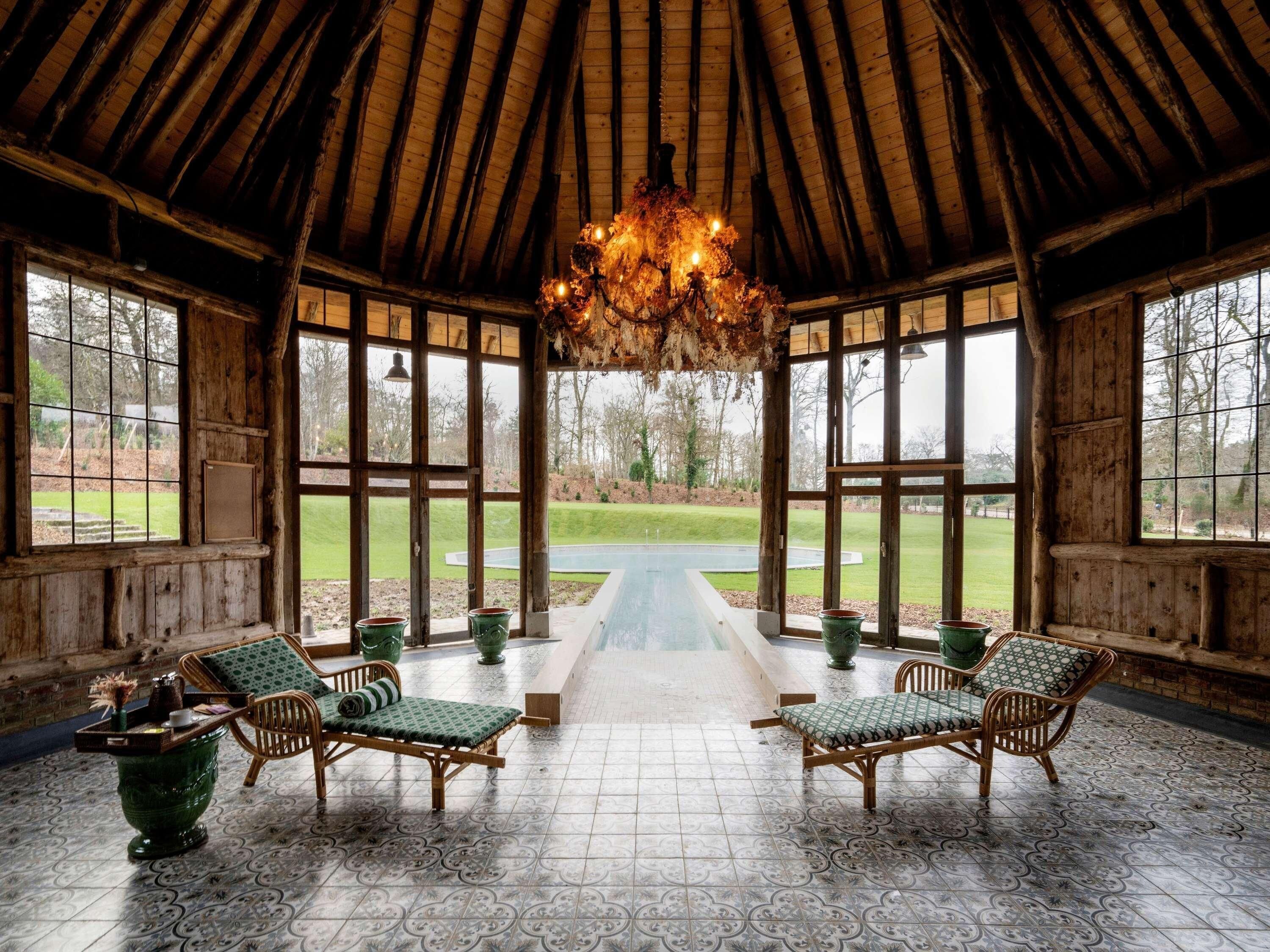A rustic wooden room with a high ceiling, large windows, and a central pathway leading to an outdoor area.