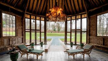 A rustic wooden room with a high ceiling, large windows, and a central pathway leading to an outdoor area.