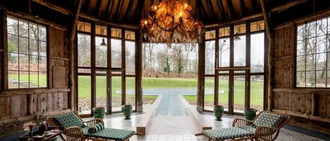 A rustic wooden room with a high ceiling, large windows, and a central pathway leading to an outdoor area.