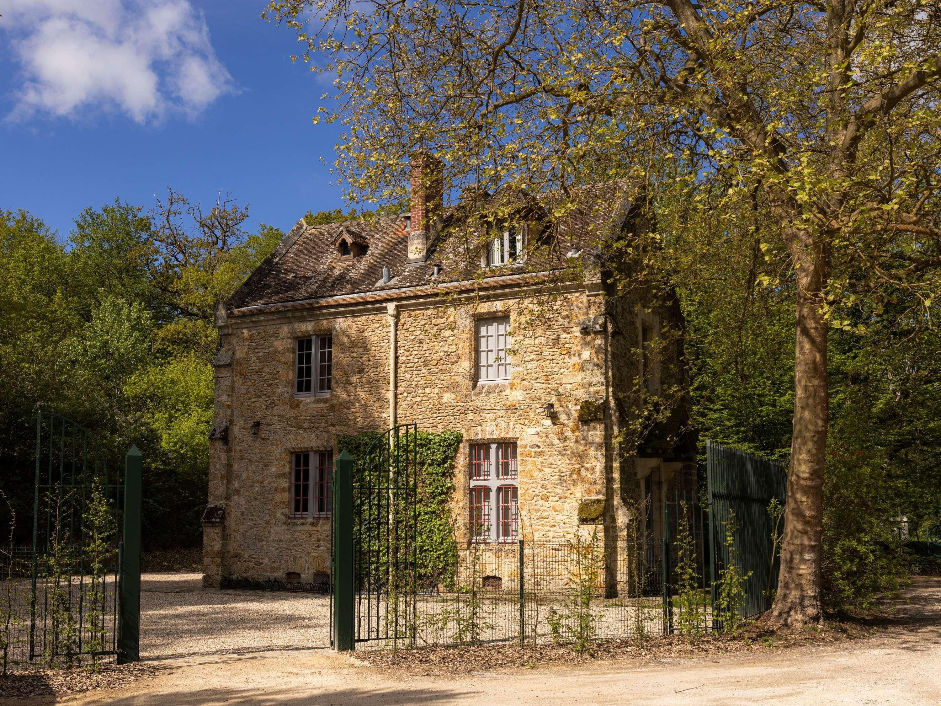 A stone building with a traditional design, surrounded by trees and a fenced area.