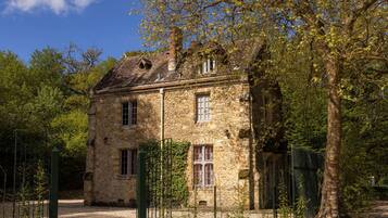 A stone building with a traditional design, surrounded by trees and a fenced area.