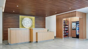 A reception area with a wooden reception desk, a wall-mounted decorative piece, and a vending machine. - Fairfield by Marriott Inn & Suites Morrow (Morrow)