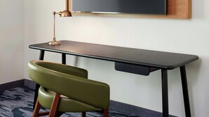 A modern desk with a black surface and wooden legs, a green chair with wooden armrests, and a wall-mounted blackboard. - Fairfield by Marriott Inn & Suites Morrow (Morrow)