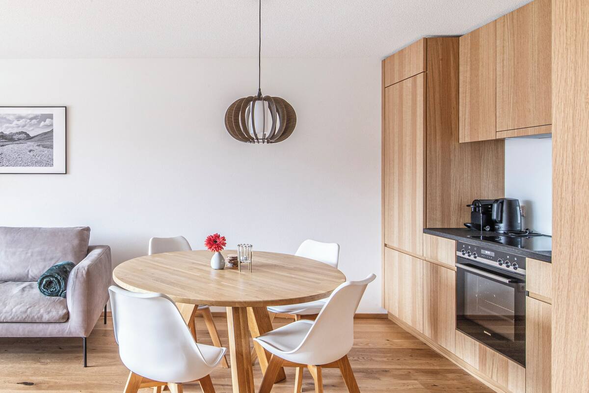 A modern kitchen with wooden cabinets, a built-in oven, and a dining area with a round table and white chairs.