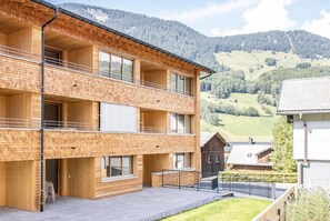 A multi-story wooden building with balconies, set against a mountainous backdrop. - Huus123 (Au)