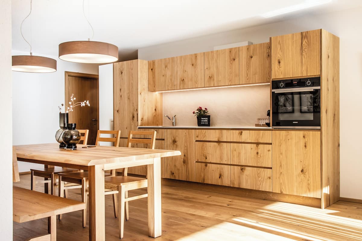 A modern kitchen with wooden cabinets, a built-in oven, and pendant lighting.