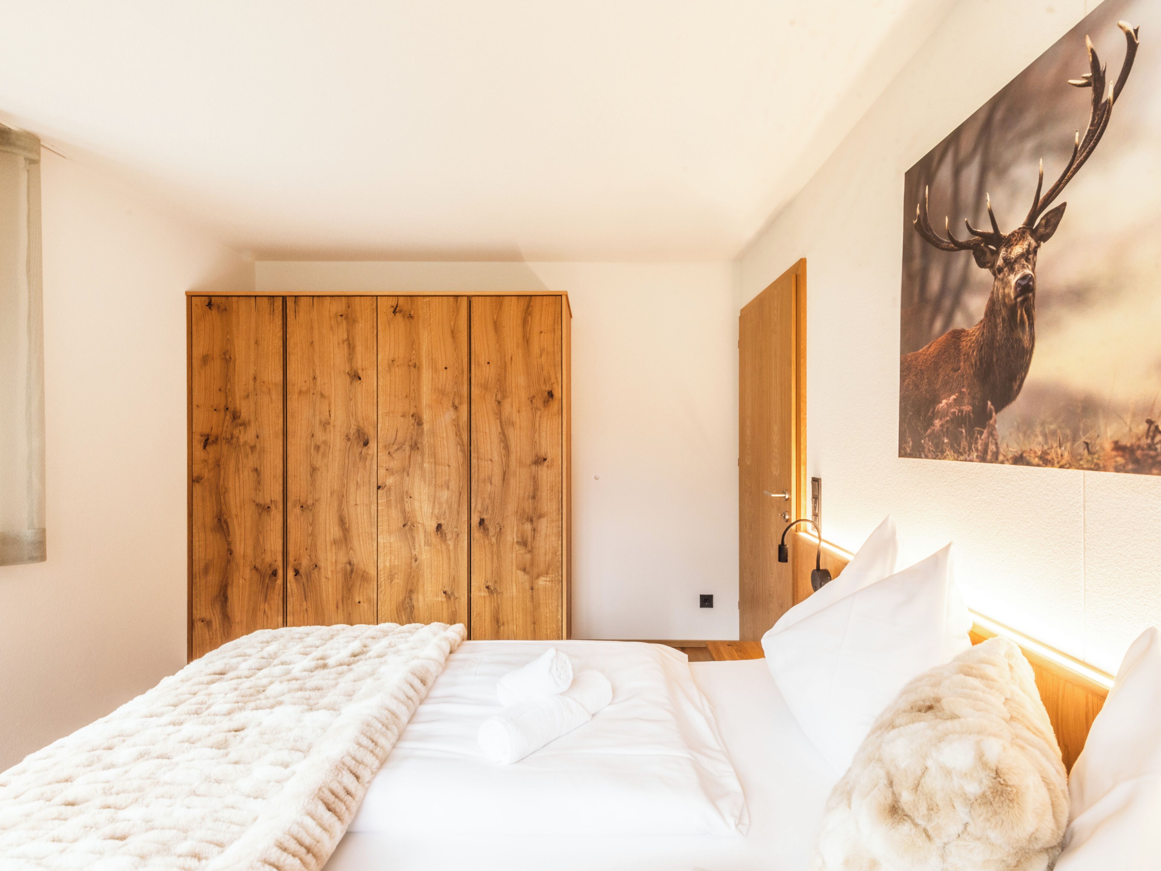 Un dormitorio con un armario de madera, una cama con ropa blanca y un cuadro de cabeza de ciervo en la pared.