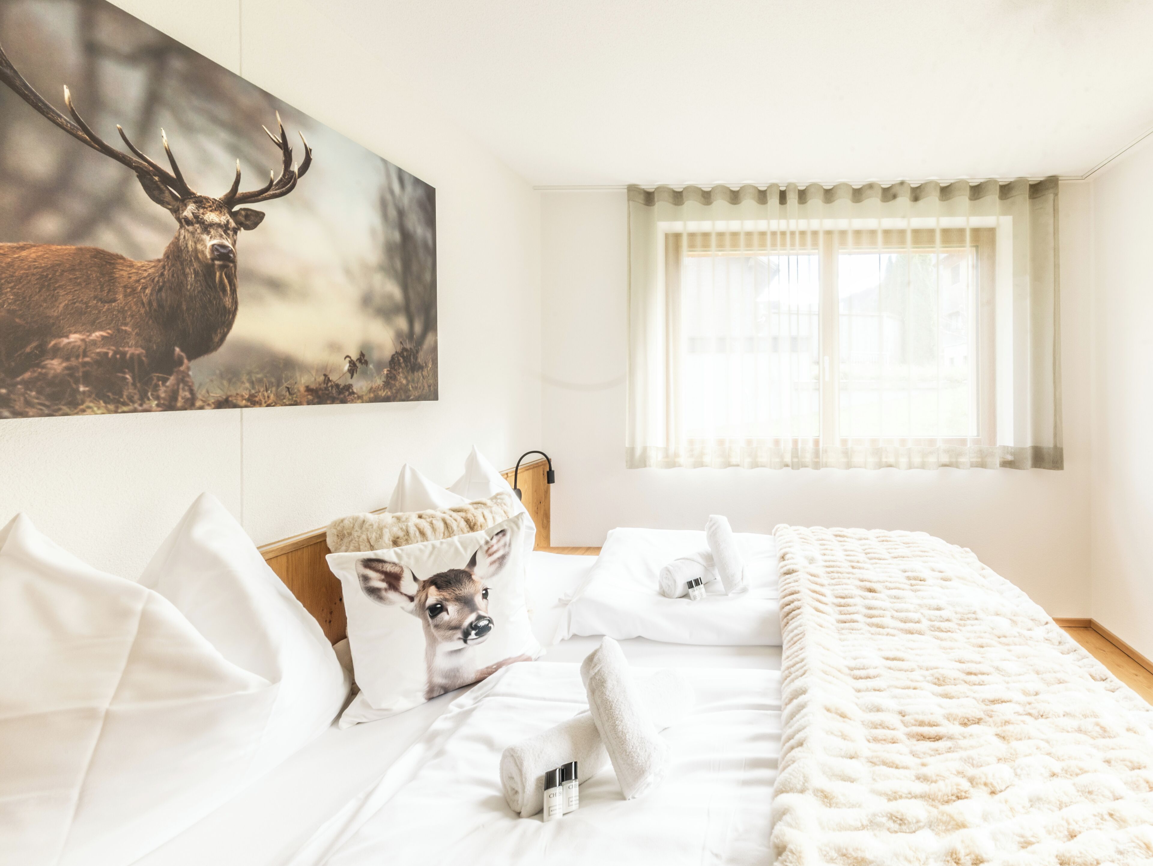 Een hotelkamer met een groot hert schilderij, een bed met witte lakens en een raam met dunne gordijnen.