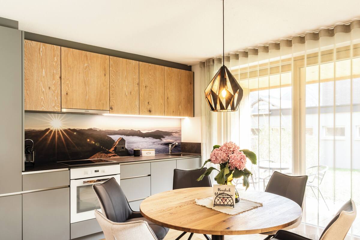 A modern kitchen with wooden cabinets, a large window, and a dining area with a round table and chairs.