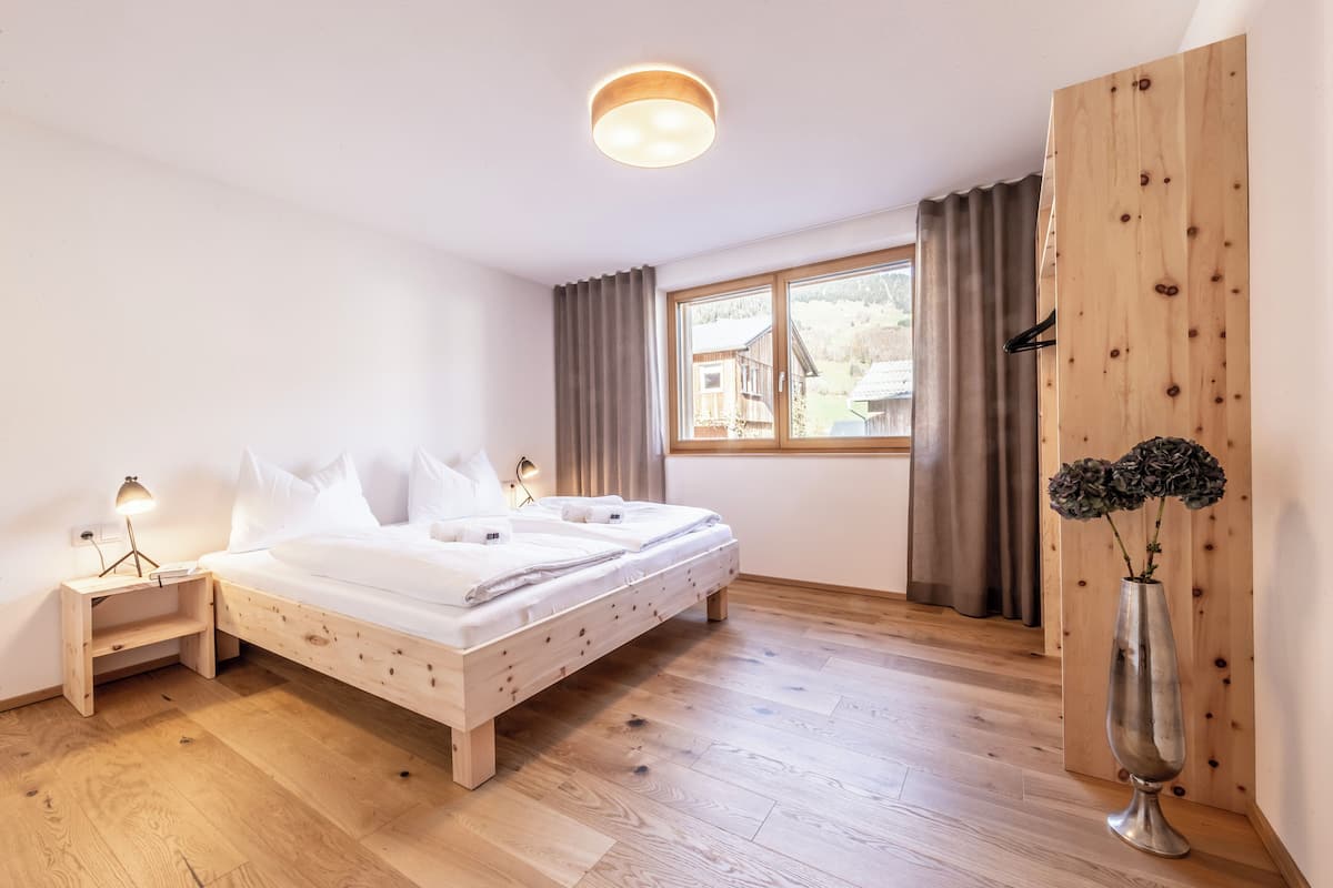 A bedroom with a wooden bed, bedside tables, a window with curtains, and a vase with flowers.