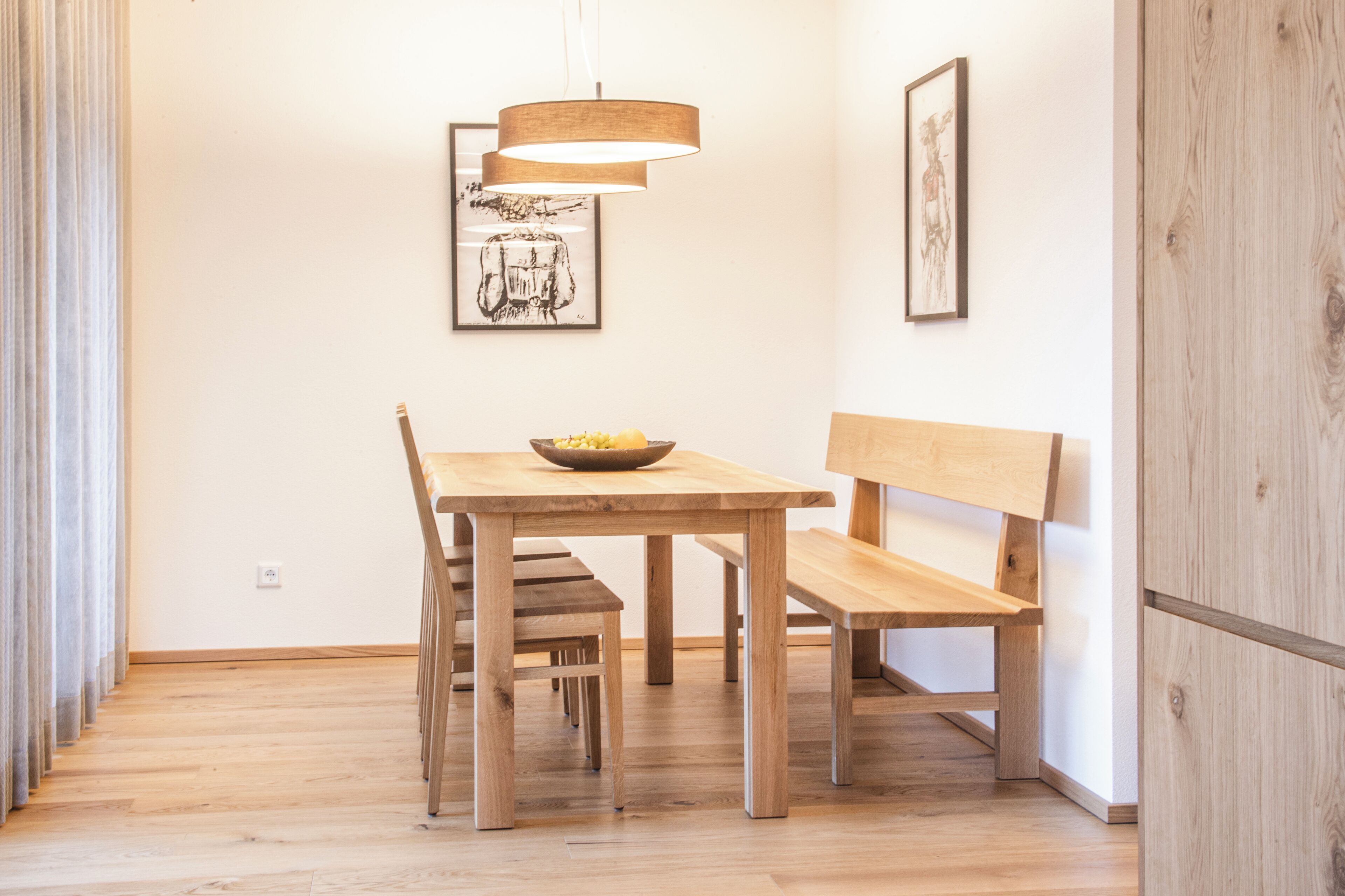 A wooden dining table with chairs, a bowl of fruit, and a hanging light fixture.