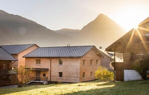 Ein Gebäude aus Ziegelsteinen mit einem geneigten Dach, umgeben von einer Rasenfläche und Bergen im Hintergrund.