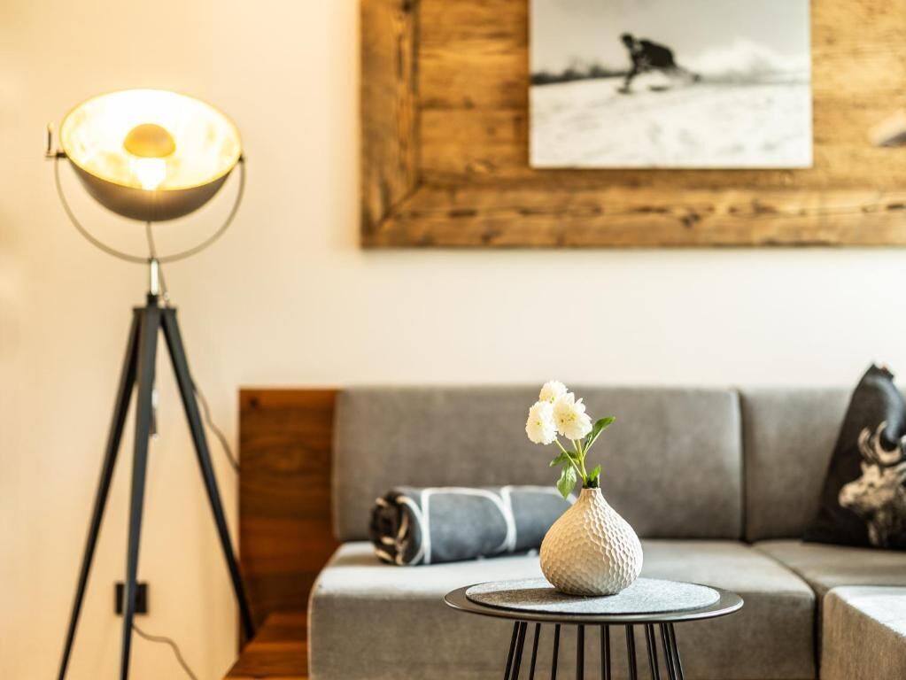 A modern living room with a sofa, a small round table with a vase of flowers, and a floor lamp.