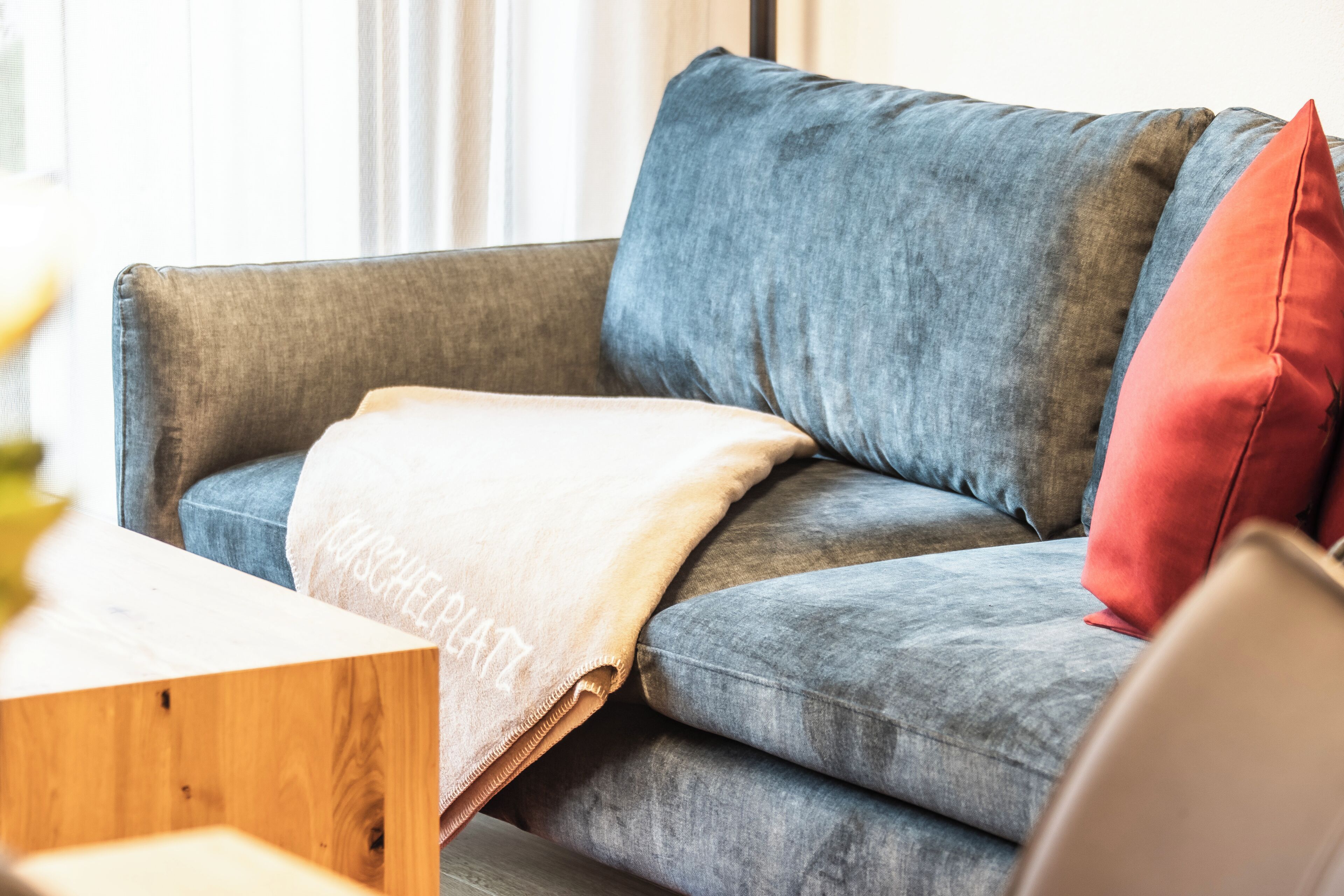 Ein graues Sofa mit einer beigen Decke und einem roten Kissen.