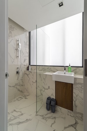 A modern bathroom with a glass shower enclosure, a white sink, and a wooden cabinet. - Lumi Tropicana by Livora Haus (Petaling Jaya)