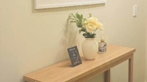 Ein hölzerner Konsolentisch mit Blumen in einer Vase und einem gerahmten Bild an der Wand.