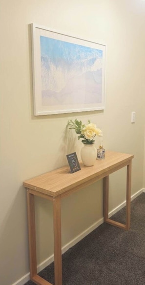 A wooden console table with a vase of flowers and a framed picture on a wall. - Stylish Tawa Retreat (Wellington)