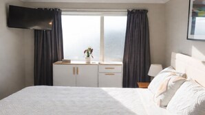 Ein Hotelzimmer mit Bett, Schreibtisch, Flachbildfernseher, Vorhängen am Fenster und Nachttischlampe.