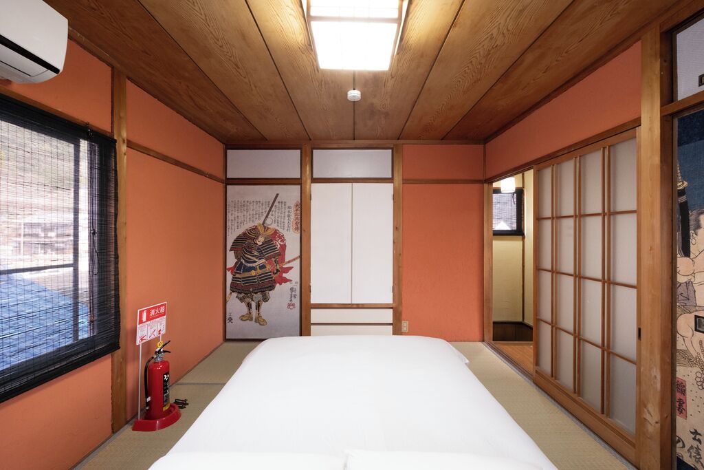 A traditional Japanese room with tatami flooring, a bed, sliding doors, and a fire extinguisher.