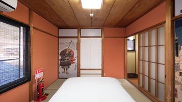 A traditional Japanese room with tatami flooring, a bed, sliding doors, and a fire extinguisher.