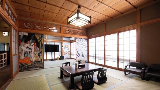 A traditional Japanese room with tatami flooring, a low wooden table, and black chairs.