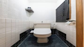 Une petite salle de bain étroite, avec des toilettes, une étagère au-dessus des toilettes et une fenêtre sur le côté droit.