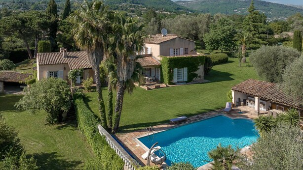 Una casa grande con piscina, rodeada de abundante vegetación y colinas al fondo.